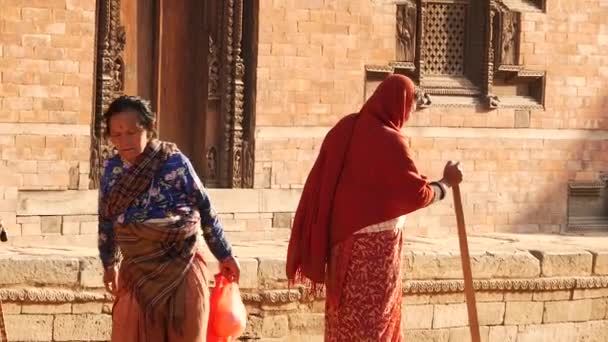 BHAKTAPUR, KATHMANDU, NEPAL - 18 Ekim 2018 Asyalı erkek ve yaşlı kadın ulusal kıyafetler içinde mutlu bir şekilde gülümsüyor, alıyor. Vatandaşlar günlük yaşam, depremden sonra antik doğu şehri. — Stok video