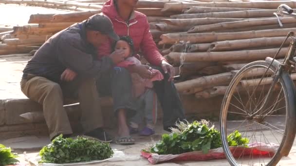 BHAKTAPUR, NEPAL - 13 DE OUTUBRO DE 2018 Homens fumando sentados com crianças na rua. Homens sentados na rua com bebê perto enquanto vendem mercadorias no mercado local. — Vídeo de Stock