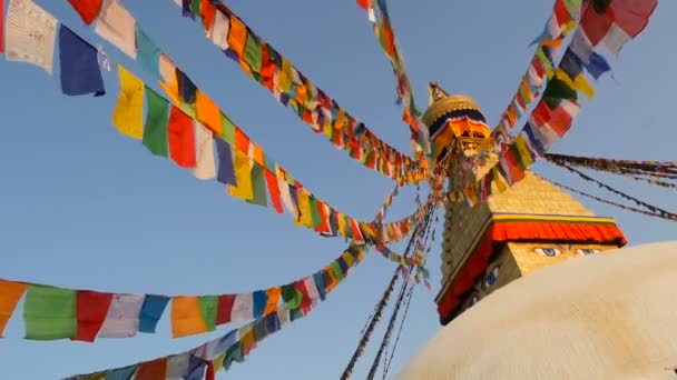Colorful prayer flags flying in the wind at Boudhanath Stupa, Holy Pagoda, symbol of Nepal and Kathmandu with golgen Buddhas Eyes. Sunset ligth — Stock Video