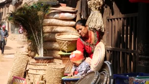 BHAKTAPUR, NEPAL - 13 OCTUBRE 2018 Mujer con niño en el patio de la casa. Mujer étnica con bebé, un montón de cestas de mimbre para la venta en la luz del sol brillante. vida cotidiana, ciudad antigua oriental después del terremoto — Vídeo de stock