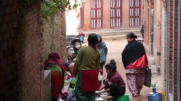 BHAKTAPUR, NEPAL - 13 OCTOBER 2018 Люди миють біля стіни храму. Жінки миють волосся і одяг водою зі старих кам'яних кранів у цегляній стіні на вулиці. Вуличне життя Катманду — стокове відео