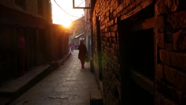 БХАКТАПУР, КАТХМАНДУ, НЕПАЛ - 18 октября 2018 года пешеходы на узкой улице на восходе солнца. Этнические мужчина и женщина ходят по пустой узкой улице рано утром. Ежедневная жизнь, восточный древний город. — стоковое видео