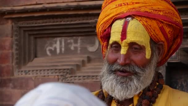 BHAKTAPUR, KATHMANDU, NEPAL - 18 Ekim 2018 Sadhu kıdemli yüzlü adam. Yaşlı Sadhu adam renkli saç bandı takıyor ve yüz rengi sofu temsilcisi. Pashipatinath. — Stok video