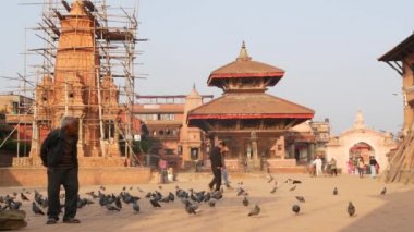 BHAKTAPUR, KATHMANDU, NEPAL - 18 Ekim 2018 Kraliyet Meydanı 'nda güvercinleri besleyen adam. Olgun bir adam antik kentteki Durbar meydanında kuşları besliyor. Günlük hayat, depremden sonra eski doğu şehri..