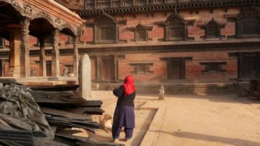 BHAKTAPUR, KATHMANDU, NEPAL - 18 Ekim 2018 Tapınak merdivenlerini süpüren yaşlı kadın. Hindu tapınağının merdivenlerini silip süpüren renkli kumaşlı yaşlı kadın. Durbar kraliyet sarayı.