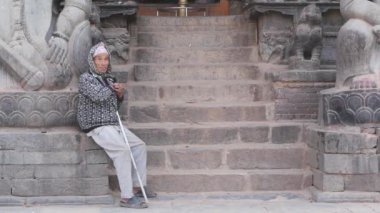 BHAKTAPUR, KATHMANDU, NEPAL - 18 Ekim 2018 Zavallı adam taş basamaklarda. Yaşlı zavallı adam Hindu tapınağının boş taş basamaklarında oturuyor. Günlük yaşam, depremden sonra doğuya ait antik şehir