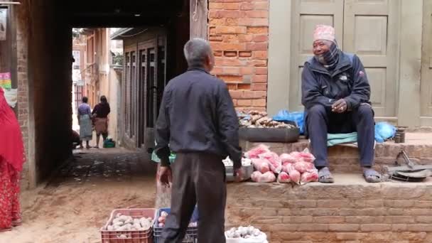 BHAKTAPUR, KATHMANDU, NEPAL - 18 oktober 2018 Livsmedelsförsäljare på tegelstaket på gatan. Man som säljer färska grönsaker på gatan sitter på tegel staket, vardag, orientalisk antik stad efter jordbävning — Stockvideo