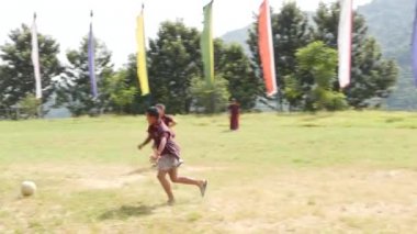 BHAKTAPUR, KATHMANDU, NEPAL - 18 Ekim 2018 Yeşil çayır üzerinde futbol oynayan Budist rahipler. Bir grup çocuk manastırı Asya 'daki tapınak bahçesinde yeşil çimlerde koşuyor..