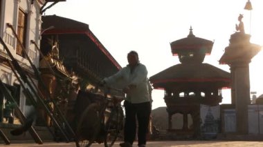 BHAKTAPUR, KATHMANDU, NEPAL - 18 Ekim 2018 Doğu antik kentinde deprem sonrası yaya trafiği. Tapınağın yakınındaki caddelerde bisiklet süren Newar 'lı bir adam.