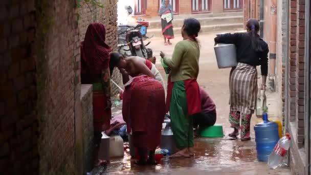 BHAKTAPUR, NEPAL - 2018. október 13.Emberek mosakodnak a templom fala közelében. Kilátás a nők mosás haj és ruhák vízzel öregített kő daruk téglafal az utcán. Kathmandu utcai élete — Stock videók