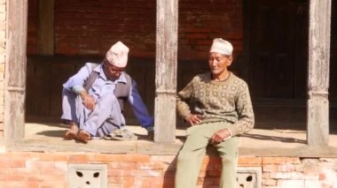 BHAKTAPUR, Katmandu, Nepal - sokakta oturan 18 Ekim 2018 yaşlı etnik adam. Çıplak ayakla ahşap terasta oturan iki yaşında etnik adam. günlük yaşam, deprem sonrası oryantal antik kenti