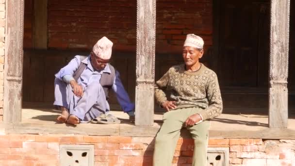Bhaktapur, Kathmandu, Nepál - 18 října 2018 starších etnické muži, sedící na ulici. Dva věku etnické muži sedí naboso na dřevěné terase. každodenní život, orientální starobylé město po zemětřesení — Stock video