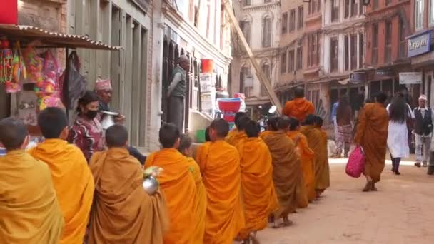 BHAKTAPUR, KATHMANDU, NEPAL - 18 de octubre de 2018 Jóvenes monjes budistas desfilan en procesión caminando por limosnas, niños recogiendo ofertas de caridad. Vida cotidiana en la calle, ciudad antigua oriental después del terremoto — Vídeo de stock
