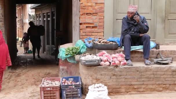 BHAKTAPUR, KATHMANDU, NEPAL - 18 жовтня 2018 Продуктор продовольства на цегляному паркані на вулиці. Людина продає свіжі овочі на вулиці сидячи на цегляному паркані, щоденному житті, у східному стародавньому місті після землетрусу. — стокове відео