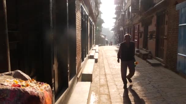 BHAKTAPUR, KATHMANDU, NEPAL - 18 oktober 2018 Voetgangers op smalle straat bij zonsopgang. Etnische man en vrouw lopen op lege smalle straat in de vroege ochtend tijd. Dagelijks leven, oosterse oude stad. — Stockvideo