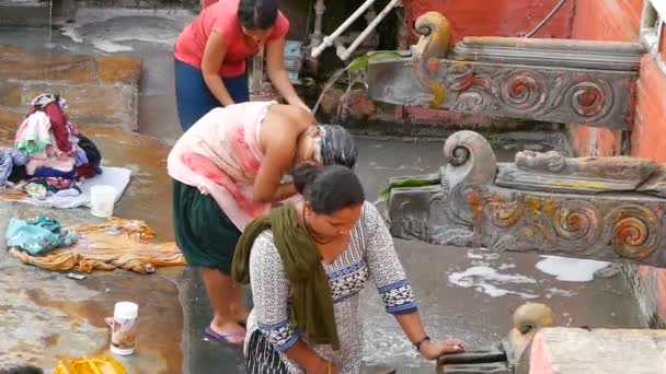 LALITPUR PATAN, NEPAL - 12 DE OUTUBRO DE 2018 Pessoas lavando perto da parede do templo. Vista de mulheres lavando cabelo e roupas com água de guindastes de pedra envelhecidos na parede de tijolo na rua. Vida de rua de Kathmandu — Vídeo de Stock