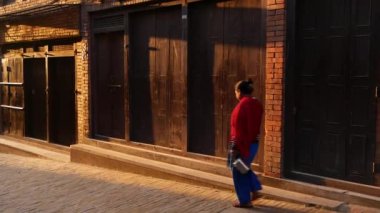 BHAKTAPUR, KATHMANDU, NEPAL - 18 Ekim 2018 Dar Sokak 'ta gün doğumunda. Sabahın erken saatlerinde boş dar bir sokakta yürüyen etnik erkek ve kadın. Günlük hayat, doğulu eski şehir.