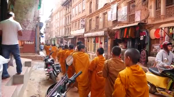 BHAKTAPUR, KATHMANDU, NEPAL - 18 de octubre de 2018 Jóvenes monjes budistas desfilan en procesión caminando por limosnas, niños recogiendo ofertas de caridad. Vida cotidiana en la calle, ciudad antigua oriental después del terremoto — Vídeo de stock