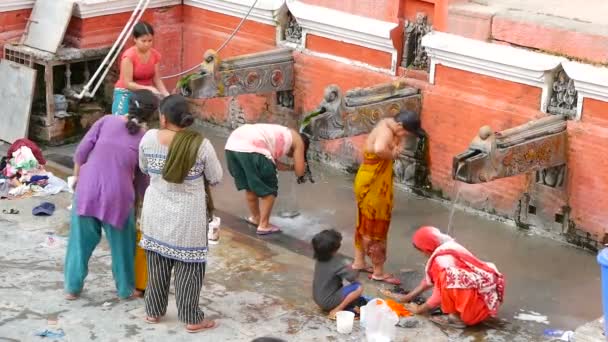 LALITPUR PATAN, NEPAL - 12 DE OUTUBRO DE 2018 Pessoas lavando perto da parede do templo. Vista de mulheres lavando cabelo e roupas com água de guindastes de pedra envelhecidos na parede de tijolo na rua. Vida de rua de Kathmandu — Vídeo de Stock