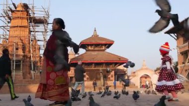 BHAKTAPUR, KATHMANDU, NEPAL - 18 Ekim 2018 Kid şehir meydanında kuşları kovalıyor. Durbar meydanında koşan ve güvercin kovalayan bir çocuk. Günlük hayat, depremden sonra eski doğu şehri..