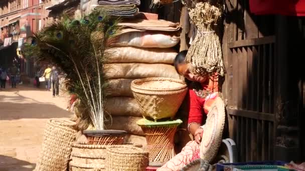 2018 년 10 월 13 일에 확인 함 . BHAKTAPUR, NEPAL - 13 OCTOBER 2018 Woman with child on house yard. 아이를 가진 민족 여성과 밝은 햇빛에 팔 수있는 많은 사악 한 바구니들. 매일의 생활, 지진이 있은 후의 고대 도시 — 비디오