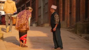 BHAKTAPUR, KATHMANDU, NEPAL - 18 Ekim 2018 Asyalı erkek ve yaşlı kadın ulusal kıyafetler içinde mutlu bir şekilde gülümsüyor, alıyor. Vatandaşlar günlük yaşam, depremden sonra antik doğu şehri.