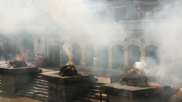KATHMANDU, NEPAL - 12. října2018. Lidé stojící na hořících ghats. Pohled na kamenné ghaty s hořící slámou a palivem v rituálu kremace u Pašupatinathu Hinduistický chrám na slunci — Stock video
