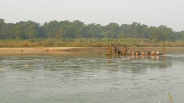 CHITWAN Ulusal Parkı, NEPAL - 10 Ekim 2018 Turistler nehirde kanoyla geziyorlar. Safari gezisi sırasında yeşil nehirde yüzen turistlerle dolu uzun tahta bir kano..