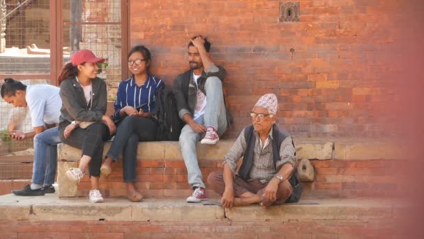 LALITPUR, NEPAL - 7 OCTUBRE 2018 Personas étnicas en la calle de la ciudad antigua, Grupo de jóvenes y hombre mayor en escalones de ladrillo en la calle de la ciudad de Patan, Khatmandu. — Vídeo de stock