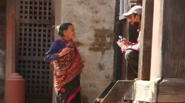 BHAKTAPUR, KATHMANDU, NEPAL - 18 Ekim 2018 Asyalı erkek ve yaşlı kadın ulusal kıyafetler içinde mutlu bir şekilde gülümsüyor, alıyor. Vatandaşlar günlük yaşam, depremden sonra antik doğu şehri.