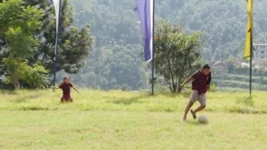 BHAKTAPUR, KATHMANDU, NEPAL - 18 Ekim 2018 Yeşil çayır üzerinde futbol oynayan Budist rahipler. Bir grup çocuk manastırı Asya 'daki tapınak bahçesinde yeşil çimlerde koşuyor..