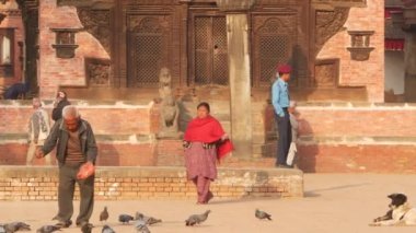 BHAKTAPUR, KATHMANDU, NEPAL - 18 Ekim 2018 Kraliyet Meydanı 'nda güvercinleri besleyen adam. Olgun bir adam antik kentteki Durbar meydanında kuşları besliyor. Günlük hayat, depremden sonra eski doğu şehri..