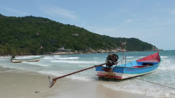 Boot an Land in der Nähe winkender See. traditionelles Boot an der Sandküste in der Nähe von wunderschönen wogenden Meer an einem sonnigen Tag auf tropischen exotischen Koh Phangan, Thailand. Vollmond Party Strand haad rin. Paradies — Stockvideo