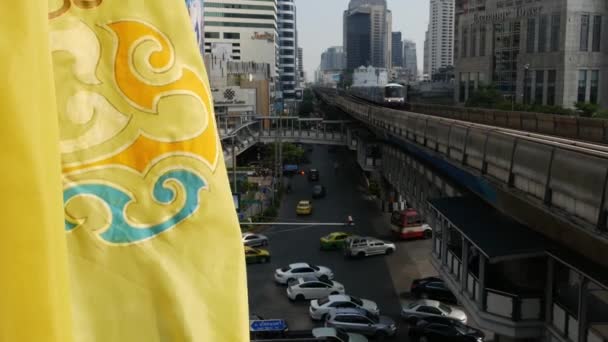 BANGKOK, TAILANDIA - 18 DE DICIEMBRE DE 2018: Tren en la calle de la ciudad. Tren moderno a caballo en el puente ferroviario sobre la carretera con coches en la calle moderna increíble. Bandera amarilla real ondeando en el viento — Vídeo de stock
