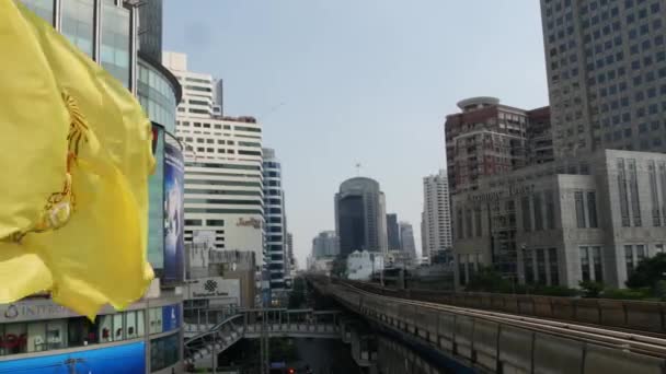 BANGKOK, THAILAND - 18 DECEMBER, 2018: Tåg ridning på stadens gata. Moderna tåg rider på järnvägsbron över vägen med bilar på fantastiska moderna gatan. Kunglig gul flagga fladdrar i vinden — Stockvideo