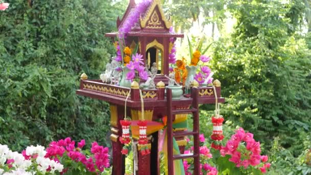 Maison d'esprit gardien miniature en bois. Petit temple bouddhiste sanctuaire, guirlandes de fleurs colorées. San phra phum érigé pour apporter la fortune. Respect traditionnel rituels animistes, cérémonies de prière — Video