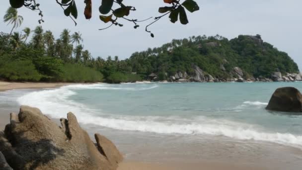 Zöld szikla a gyönyörű tenger közelében. Fenséges kék tenger hullámzik közel durva zöld szikla Ko Phangan napsütéses napon Thaiföldön. Egzotikus trópusi paradicsomi strand. — Stock videók