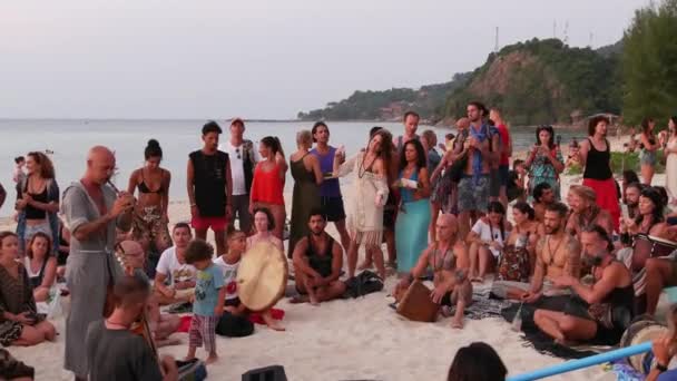 泰国帕岸岛-2019年2月23日禅宗海滩。快乐的人在日落时在热带天堂夏季海岸上弹吉他和鼓, 周围有许多人。音乐障碍, 自由概念, 社交休闲 — 图库视频影像