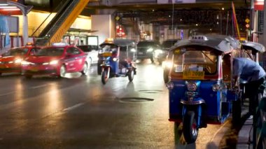 BANGKOK, THAILAND - 18 ARALIK 2018: Geleneksel Tayland taksisi - Tuk Tuk yol boyunca turistleri bekliyor. Kalabalık şehrin gece trafiği. Asya ülkesinin sembolü, eşsiz bir araç.
