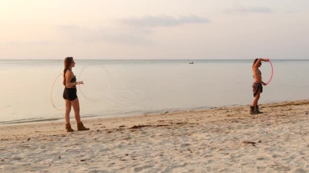 Koh Phangan, Tayland - 11 Ocak 2019 Denize yakın plajda fitness çemberleri ile genç bayanlar. Gün batımında su kenarında kum kıyısında yürüyen jimnastik çemberleri ile genç bayanlar yan görünümü. — Stok video