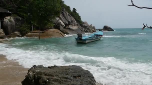 Boot op de wal in de buurt van golvende zee. Traditionele boot gelegen aan de zanderige kust in de buurt prachtige golvende zee op zonnige dag op tropische exotische Koh Phangan, Thailand. Full moonparty strand Haad Rin. Paradijs — Stockvideo
