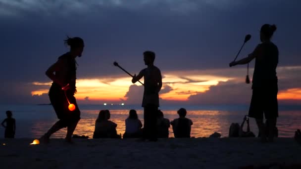 パンガン島、タイ- 23 3月2019禅ビーチ。日没時にビーチで演奏者のシルエット。穏やかな海と日没の空に対して砂浜でリハーサルする若い無名のエンターテイナーのシルエット. — ストック動画