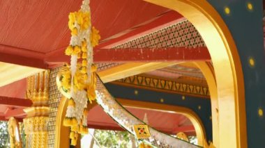 Oryantal yapıçiçek süslemeleri. Tayland güneşli bir günde tomurcuklanmış tapınağın süs binasının tavanına asılı güzel çiçek kompozisyonları
