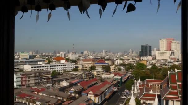 Cityscape of modern oriental town. View from the window of houses roofs on streets of majestic Bangkok from Golden Mount Temple during sunset time. Traditional metal bells with wishes hanging — Stock Video