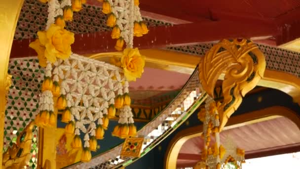 Decoraciones florales de edificio oriental. Hermosas composiciones de flores colgando en el techo del edificio ornamental del templo budista en el día soleado en Tailandia — Vídeos de Stock