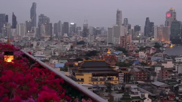 Pohled na tradiční a moderní budovy orientálního města. Krásné květinové záhony proti městskému prostředí tradičních domů a mrakodrapů v zamlžený den v ulicích Bangkoku nebo Krungtepu. — Stock video