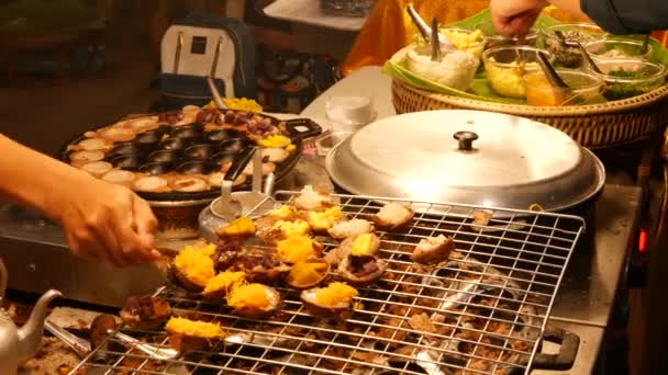 Exotiska orientaliska asiatiska söta läckra desserter, ovanliga färgglada traditionella rätter på diskarna i en basar med gatumat. Kvällsmat i bangkok, huvudstaden i matlagning. Nattmarknad — Stockvideo