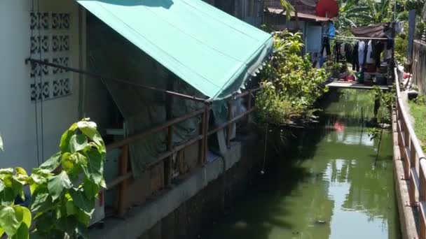 Orientalisk slum nära kanalen. Shabby hus av typiska orientaliska slum ligger nära liten kanal på gatan i Bangkok på solig dag. Dåligt traditionellt boende nära vatten i hus på styltor. — Stockvideo