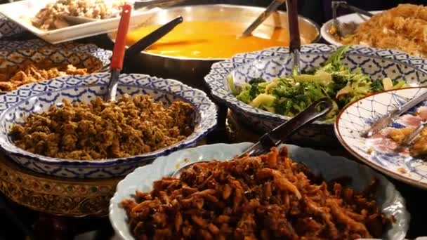 Cuencos con varios platos asiáticos en el puesto. Cuencos de surtidos platos tradicionales tailandeses colocados en el puesto de comedor de la calle por la noche. Mercado nocturno oriental patio de comidas. — Vídeos de Stock