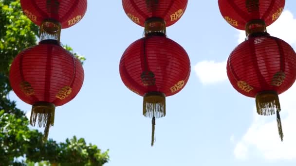 Linternas de papel en un edificio de mala calidad. Linternas de papel rojo colgando en el techo del edificio del templo de hormigón envejecido en el día soleado entre la vegetación jugosa en el país oriental. decoración tradicional — Vídeos de Stock